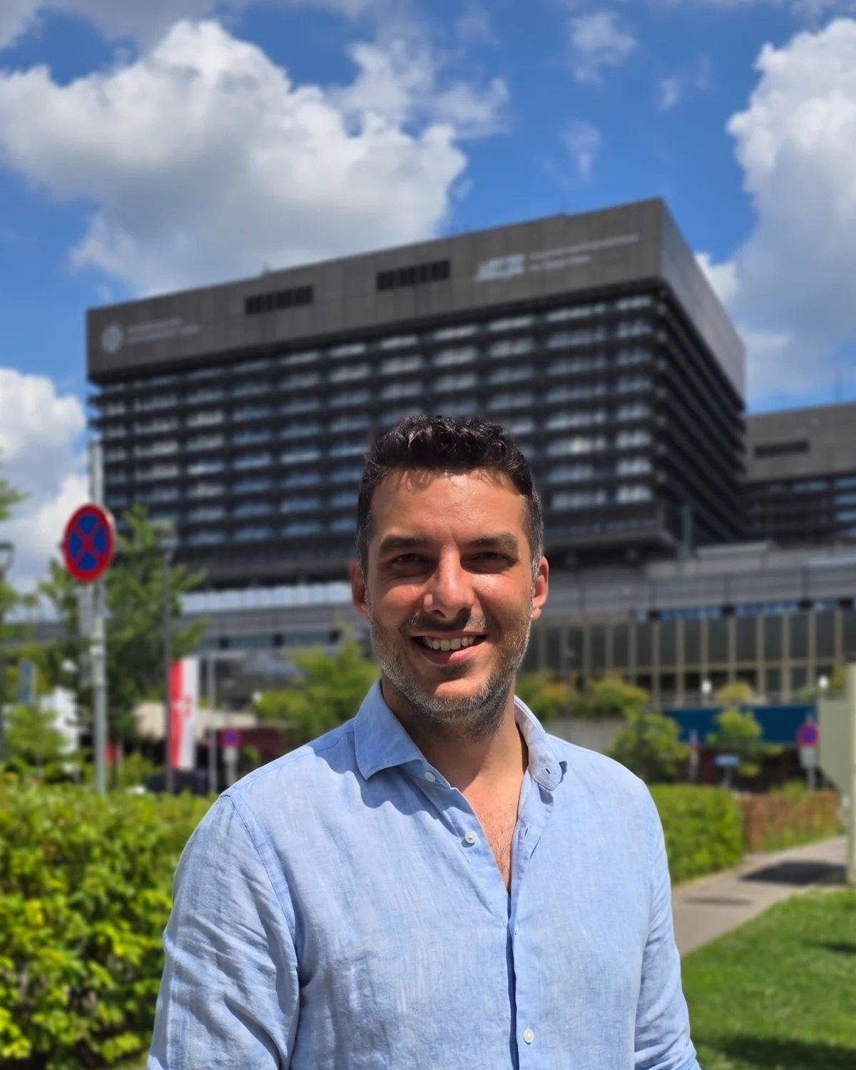 Marius Oncescu, navigator medical, zâmbind în fața spitalului AKH din Viena, cu laptopul sub braț